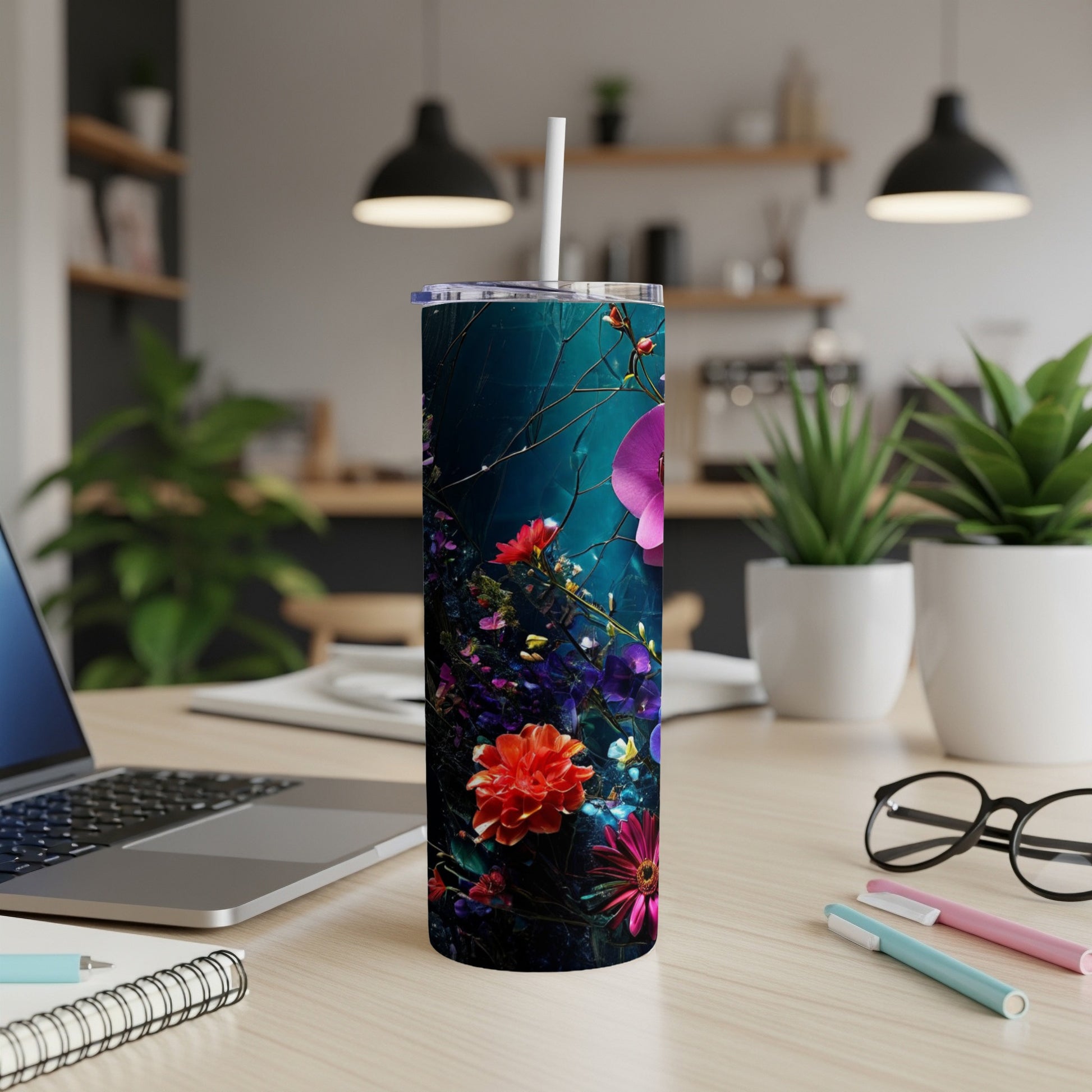 Tall tumbler with dark floral pattern on desk with laptop and pens.