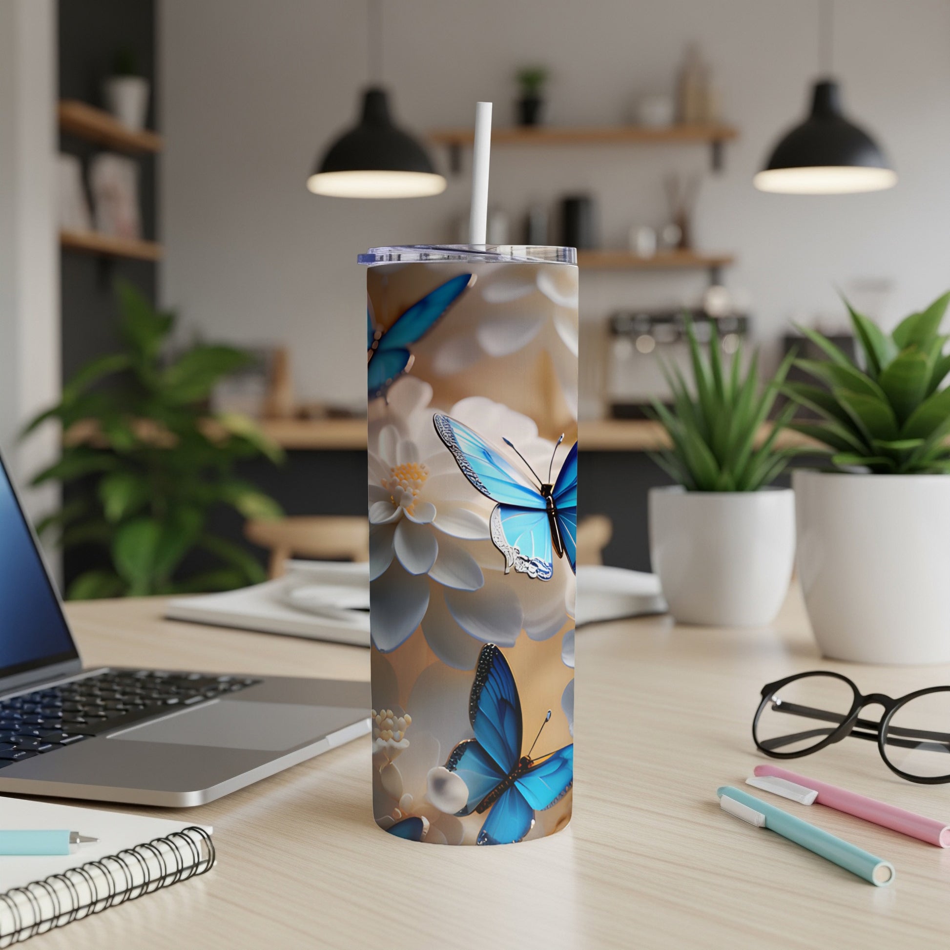Tall tumbler with blue butterflies and white flowers on a desk.