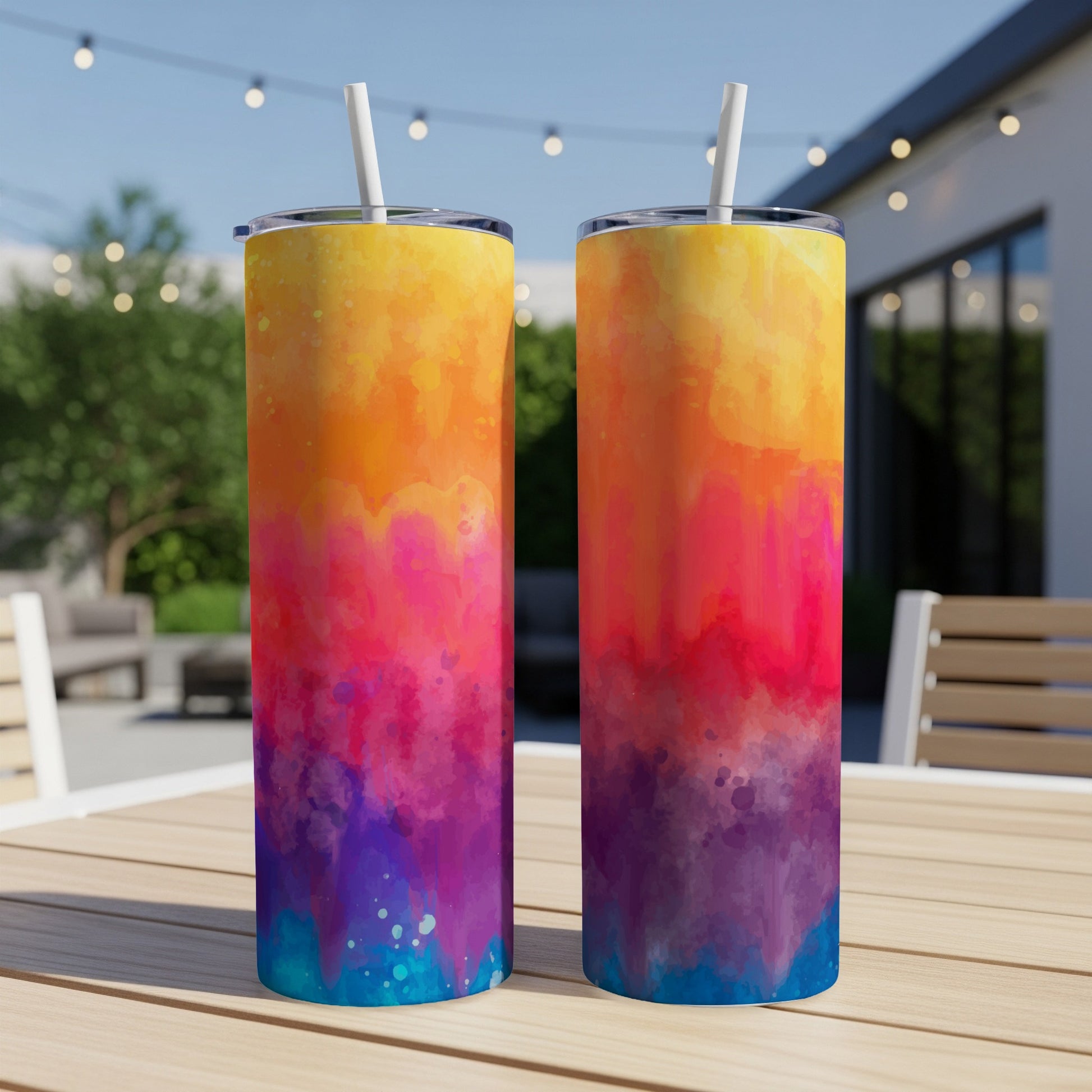 Two tumblers with watercolor designs in orange, pink, purple, and blue on a table outdoors.