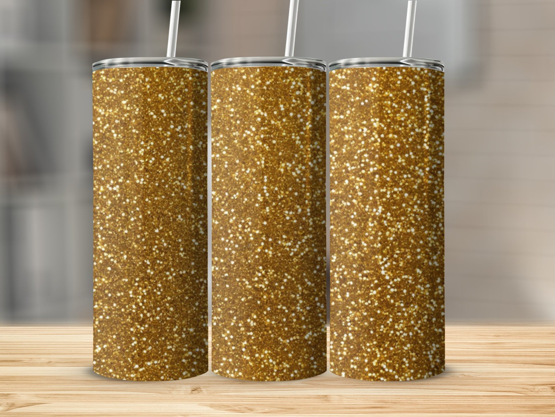 Three gold glitter tumblers with straws on a wooden surface.