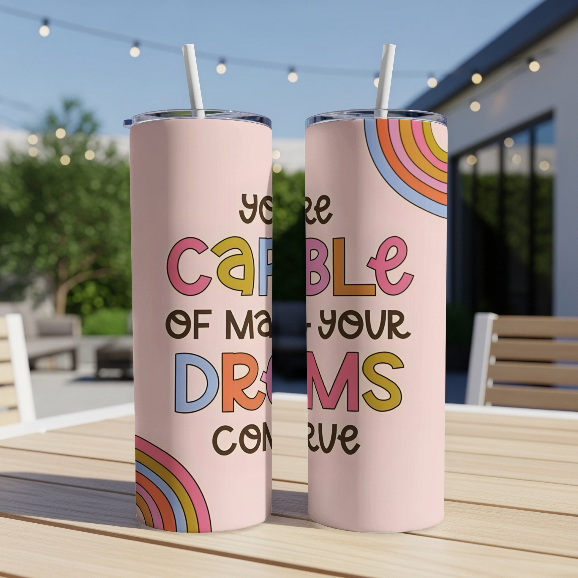 Pink tumbler with rainbow accents and text "you're capable of making your dreams come true".