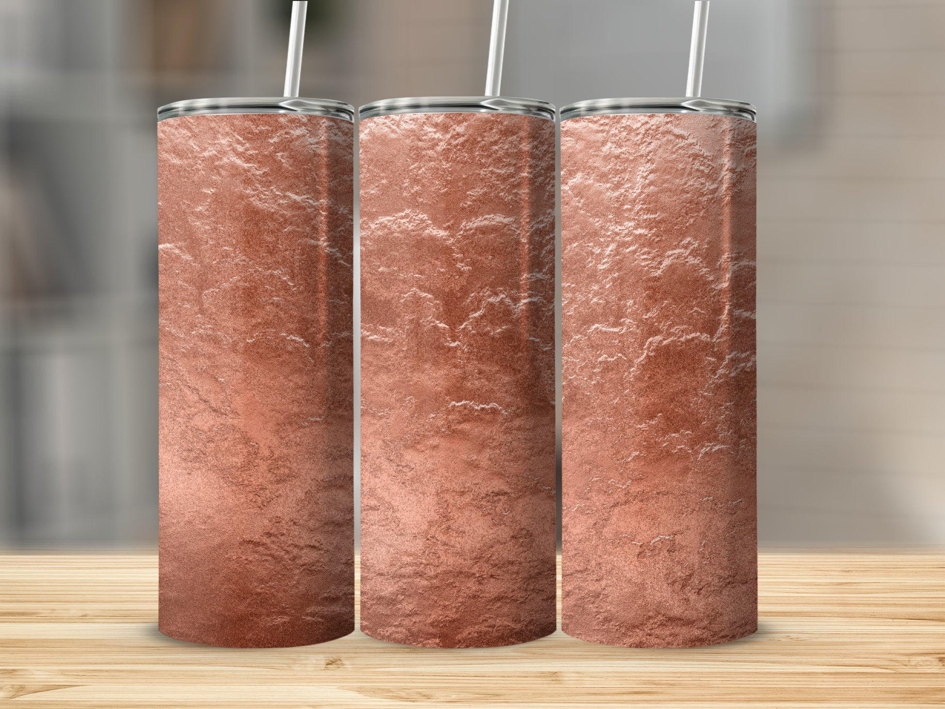 Three rose gold textured tumblers with straws on a wooden surface.