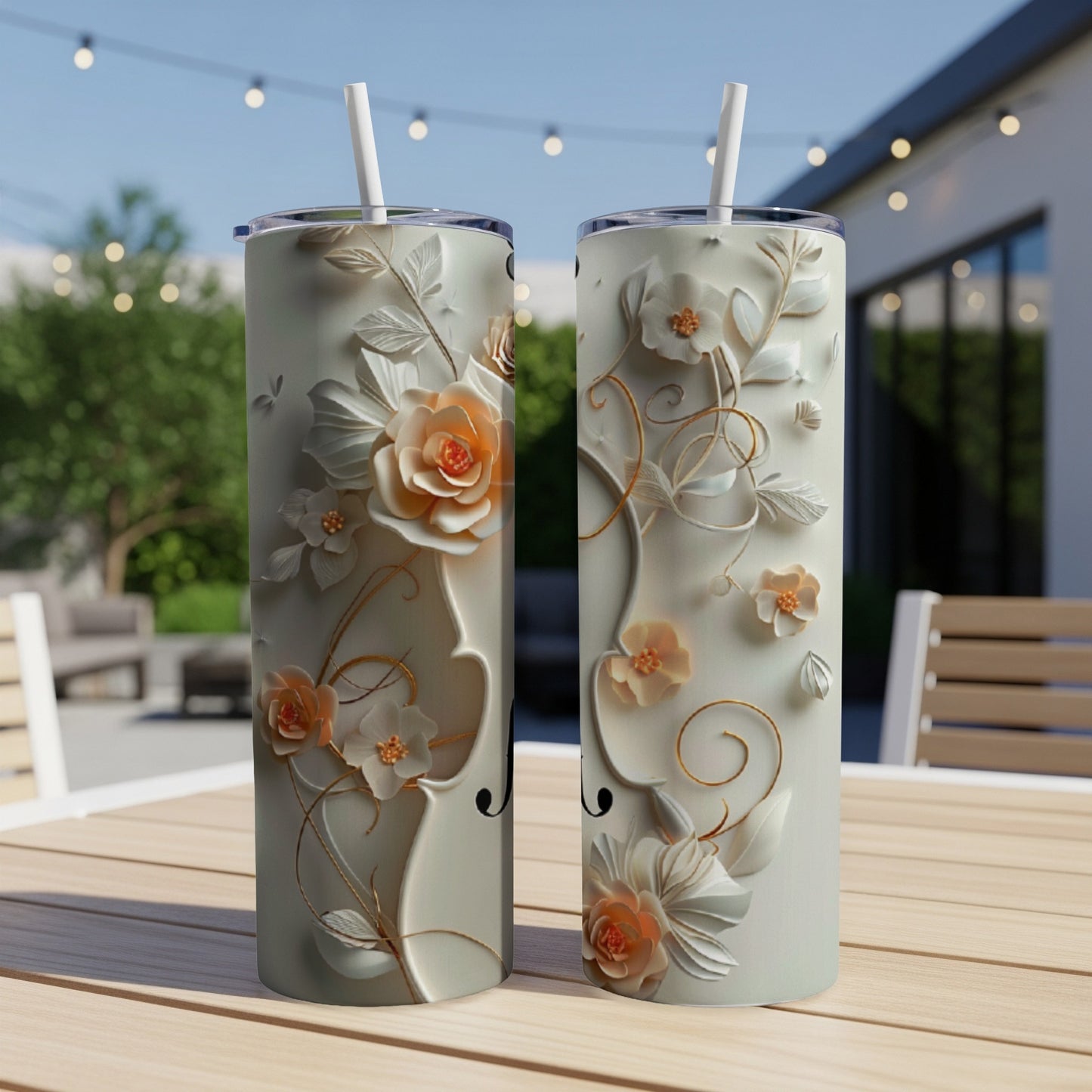 Two tall tumblers with raised floral designs and straw on an outdoor table.