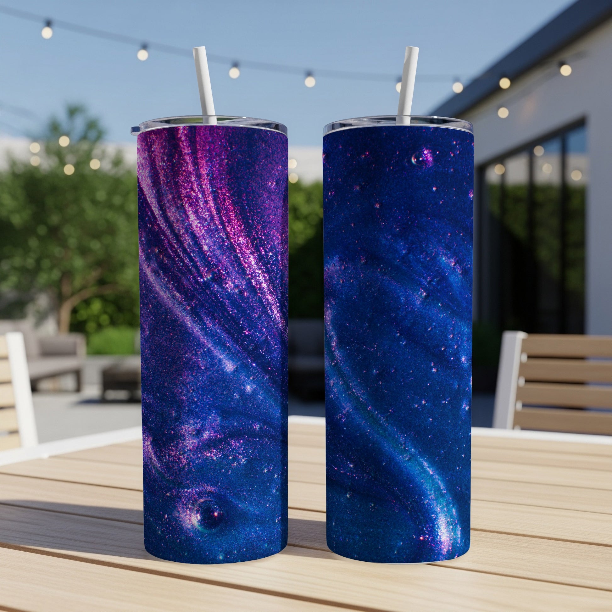 Two tumblers with a swirling galaxy design sit on a wooden table outdoors.