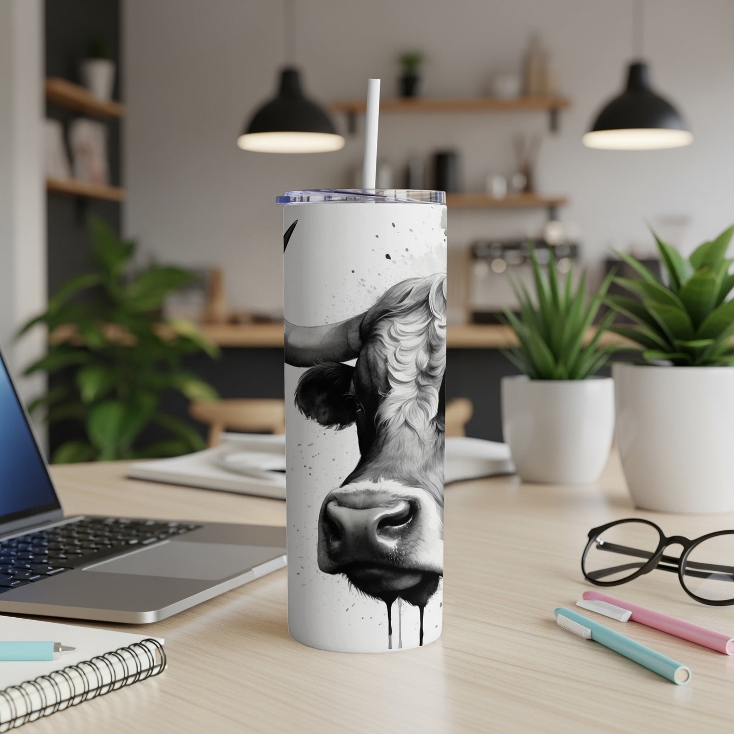 Black and white cow portrait on a tumbler with a straw, on a desk.