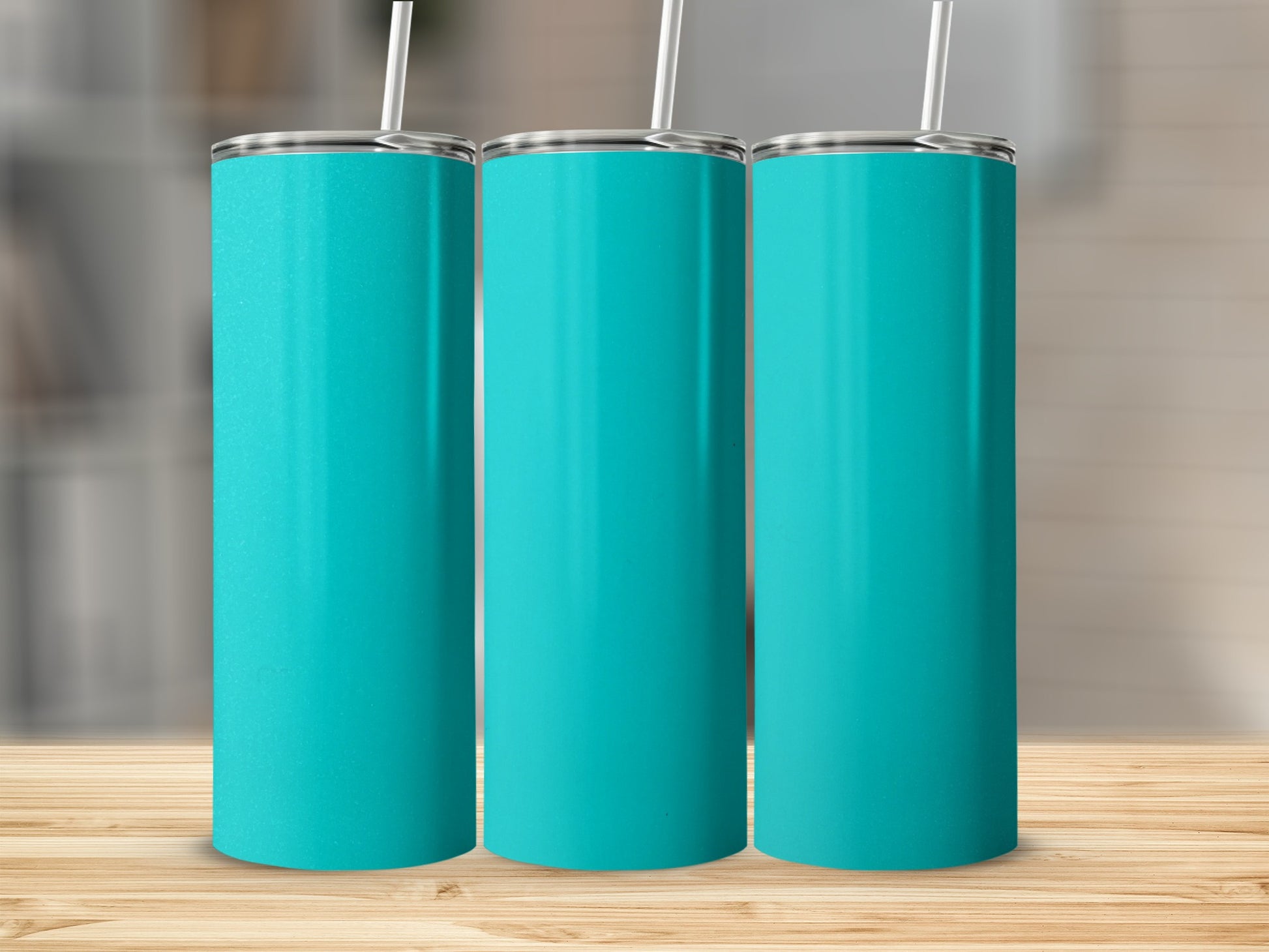 Three teal tumblers with straws stand on a wooden surface.