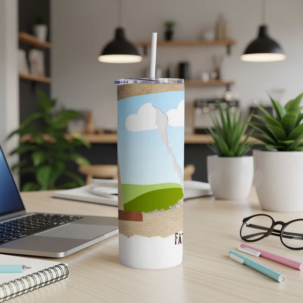 Tumbler with landscape graphic and straw, on a desk with laptop and glasses.