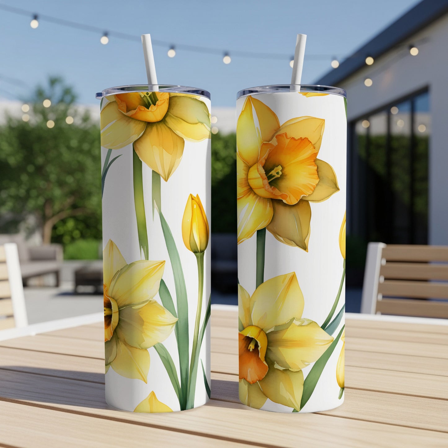 Two white tumblers with yellow daffodils pattern, on outdoor table.