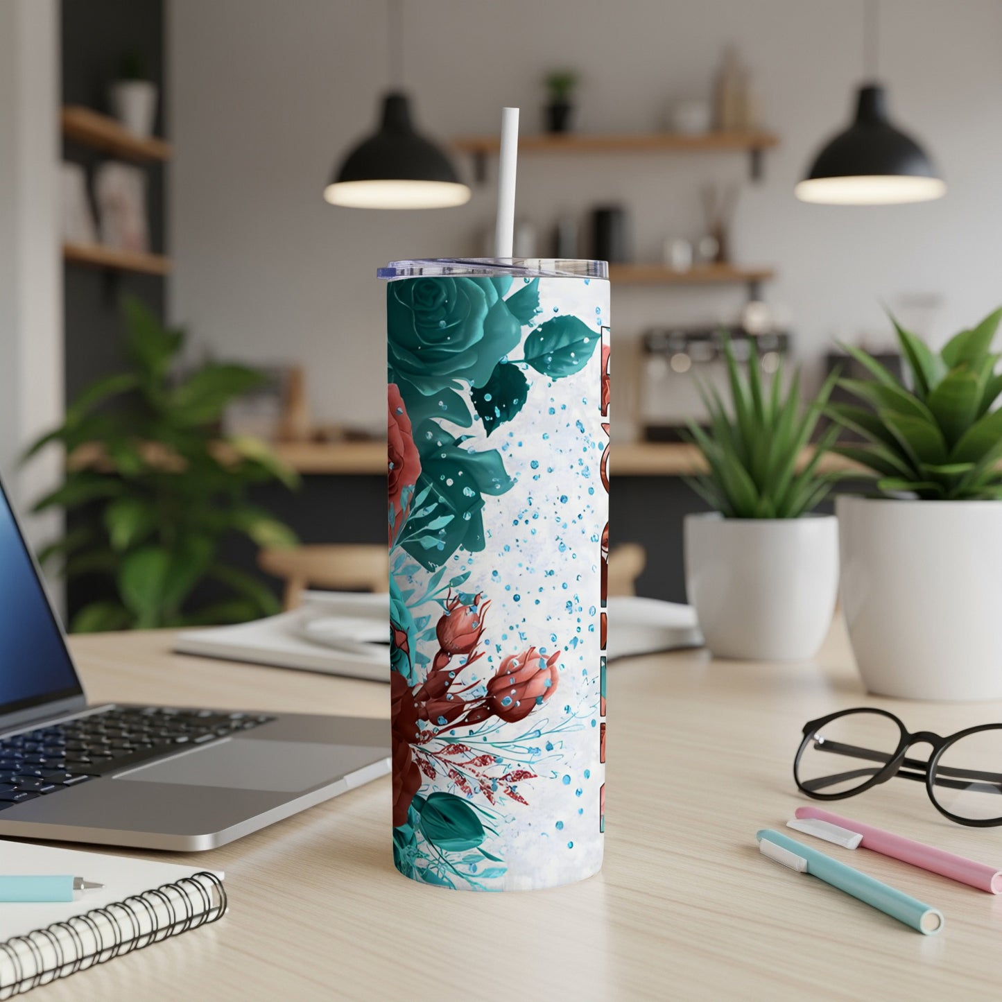 White tumbler with teal and red floral design and straw on desk.
