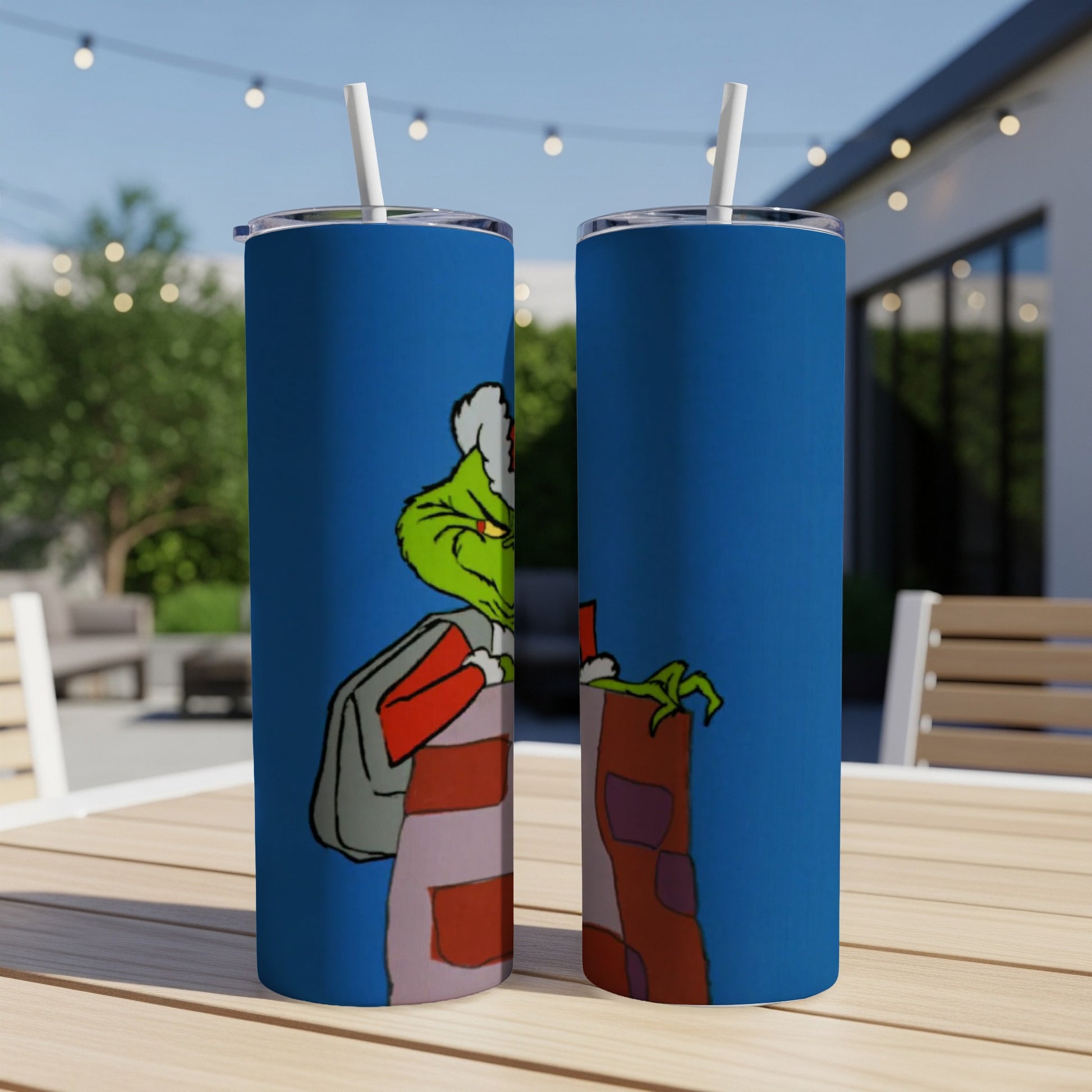Grinch character on blue tumblers with straws on an outdoor table.