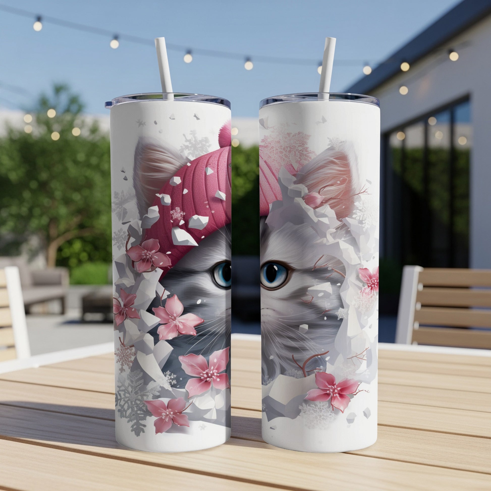 Two tumblers with a close-up of a cat wearing a pink beanie, surrounded by pink flowers and snowflakes.