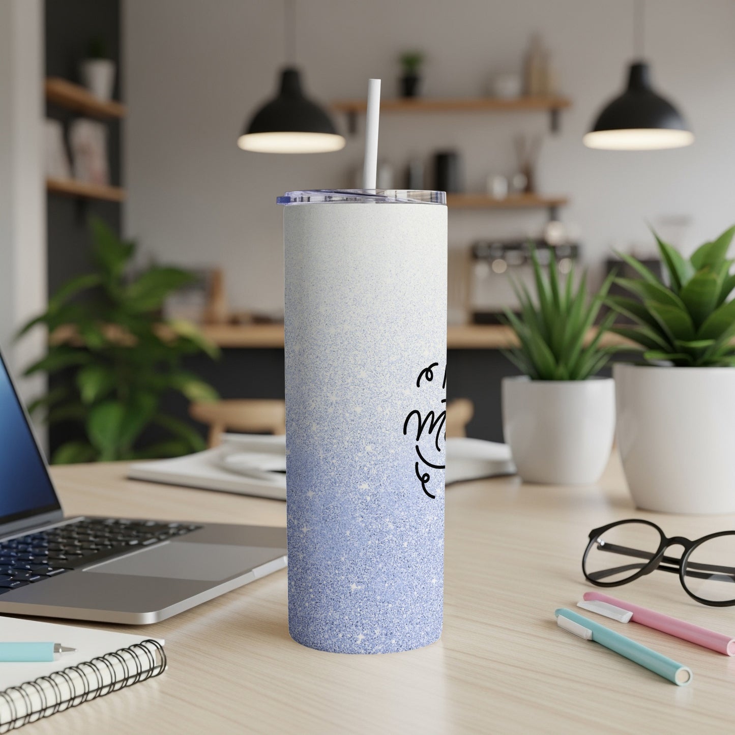 Glittering blue tumbler with "mom" in cursive, on a desk with laptop.