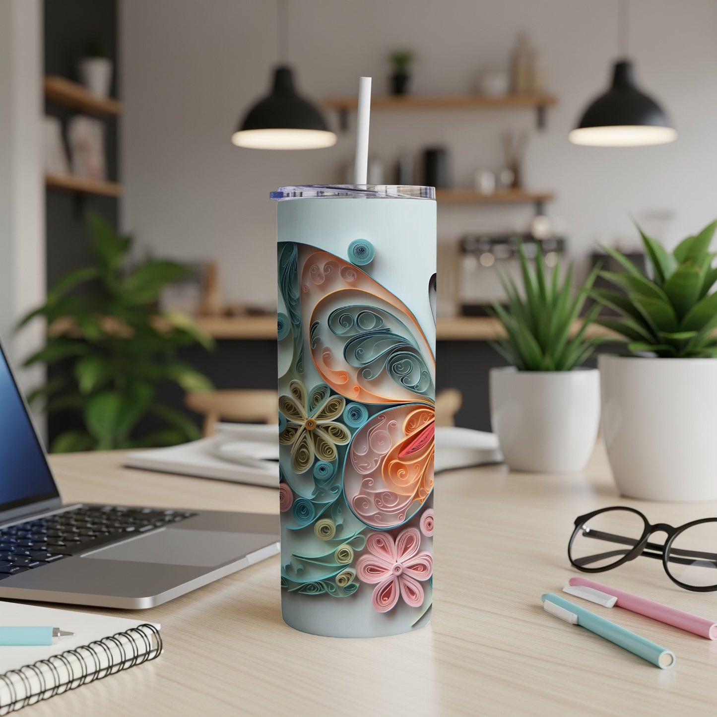 Light blue tumbler with quilled paper butterfly and flower art on a desk.