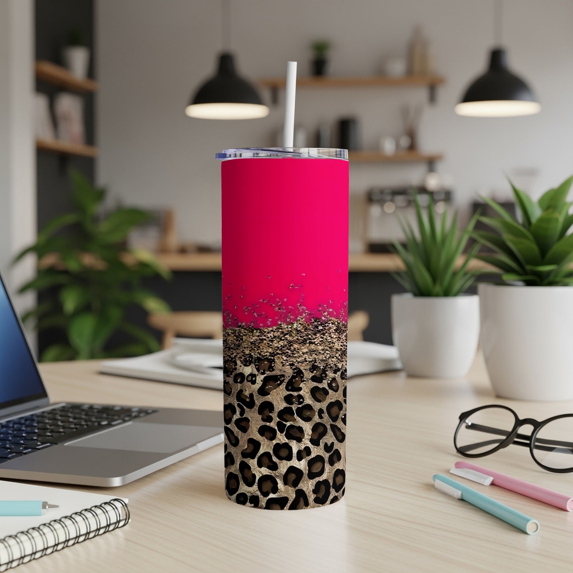 Pink and leopard print tumbler with straw on desk with laptop and pens.