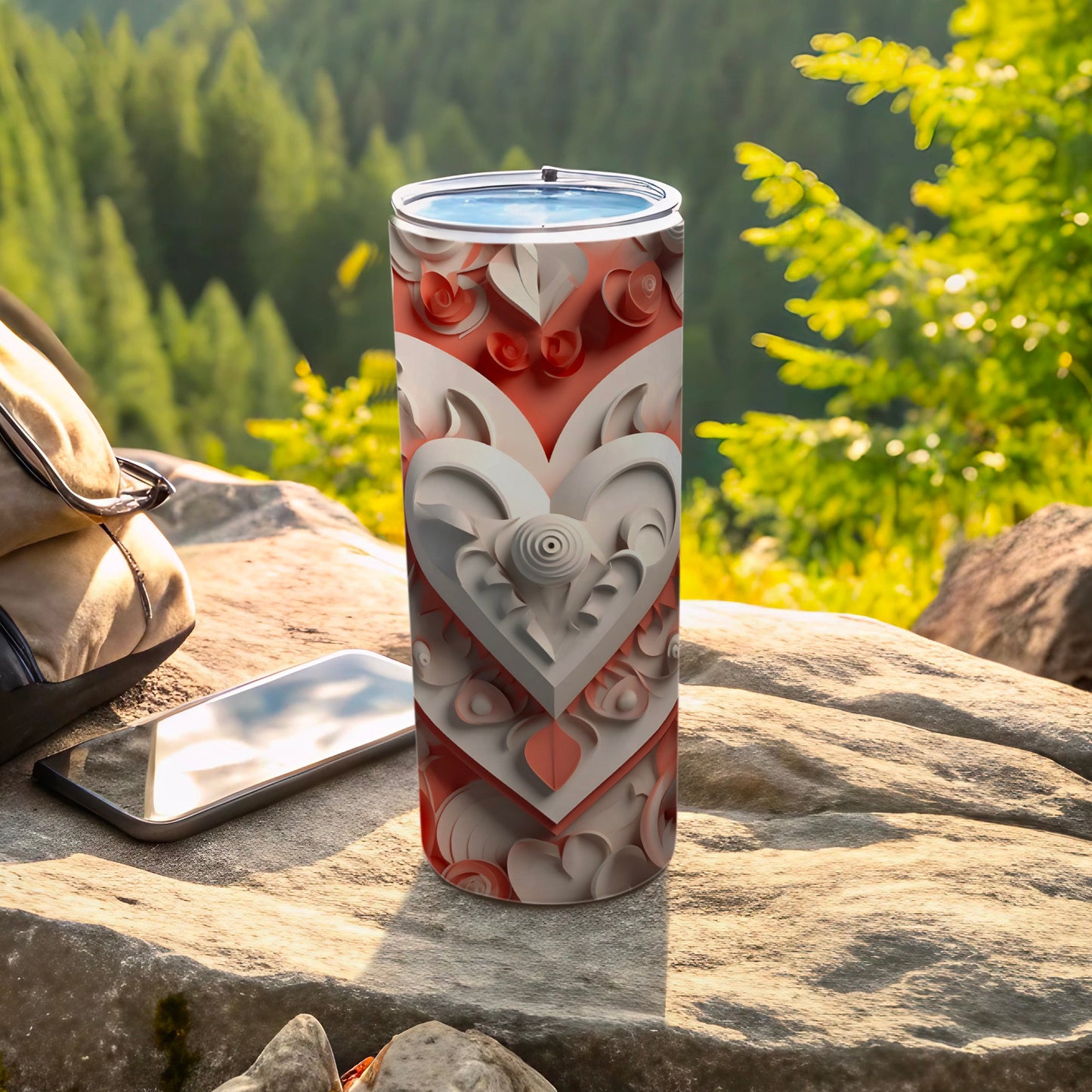 White and red heart pattern tumbler on rocks with phone and bag.
