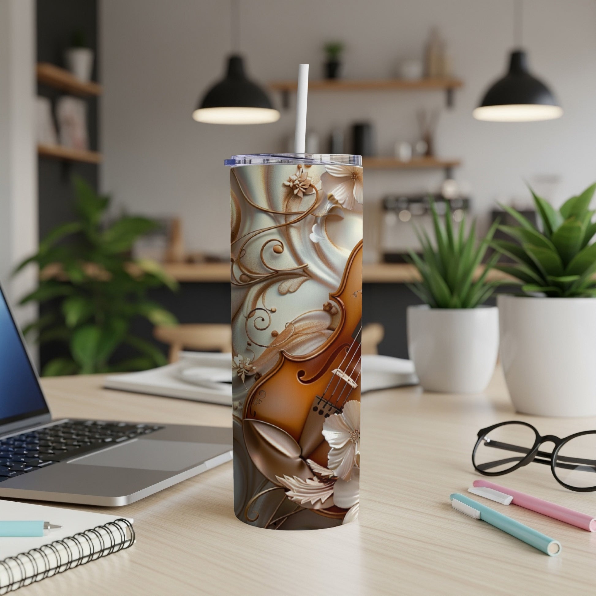 Tall tumbler with ornate floral violin design and straw, on a desk.