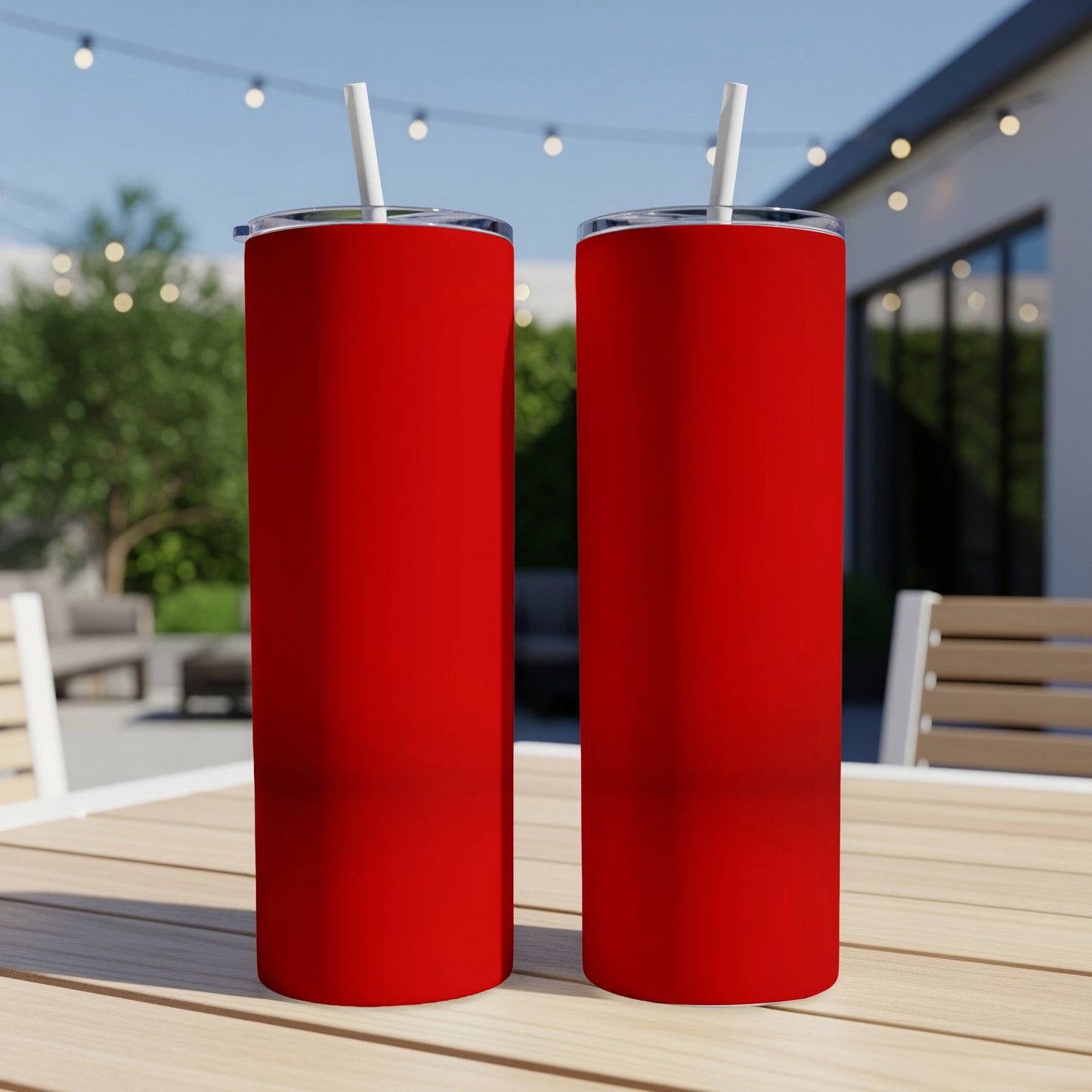 Two red tumblers with white straws on a wooden table outdoors.