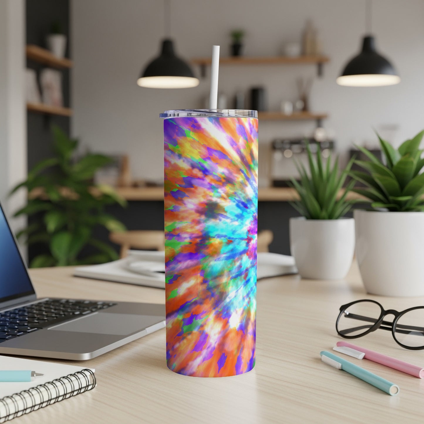 Tumbler with colorful tie-dye pattern and straw, on a desk with laptop.