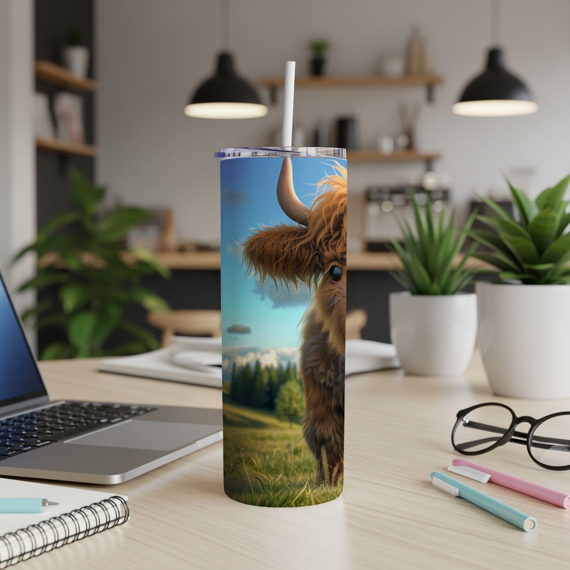 Highland cow illustration on a tumbler, with laptop and pens on desk.