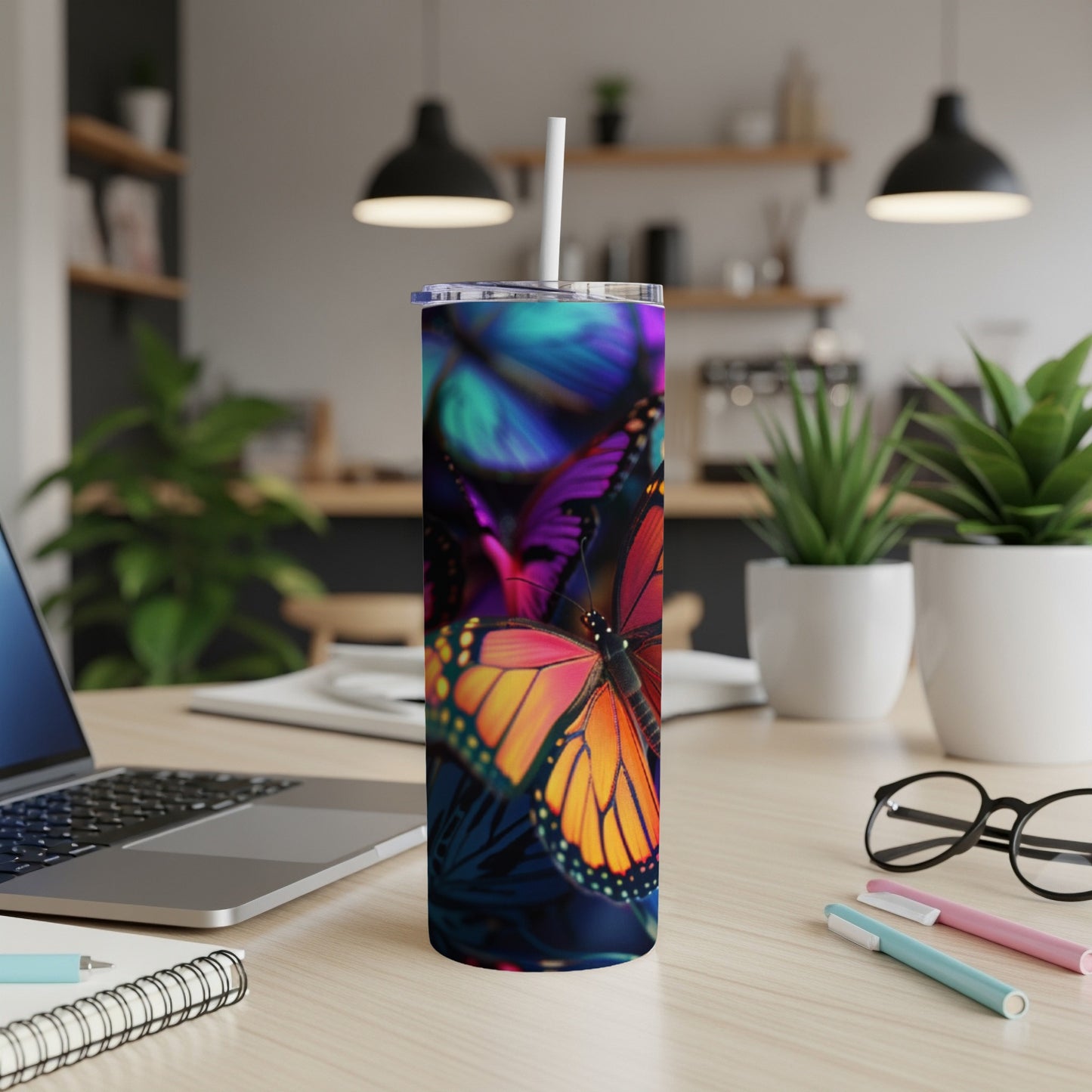 Tumbler with colorful butterflies, laptop, and pens on a desk.