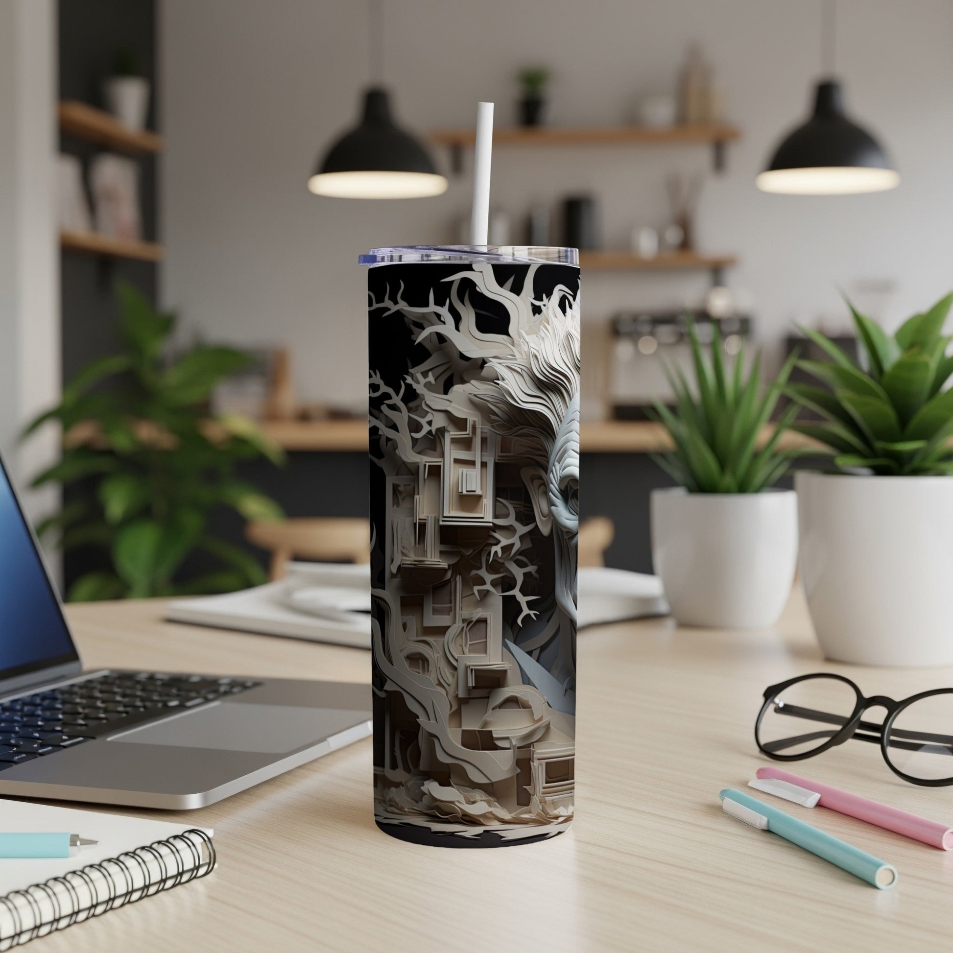 Tumbler with monochrome abstract paper cut design and straw on a wooden desk.