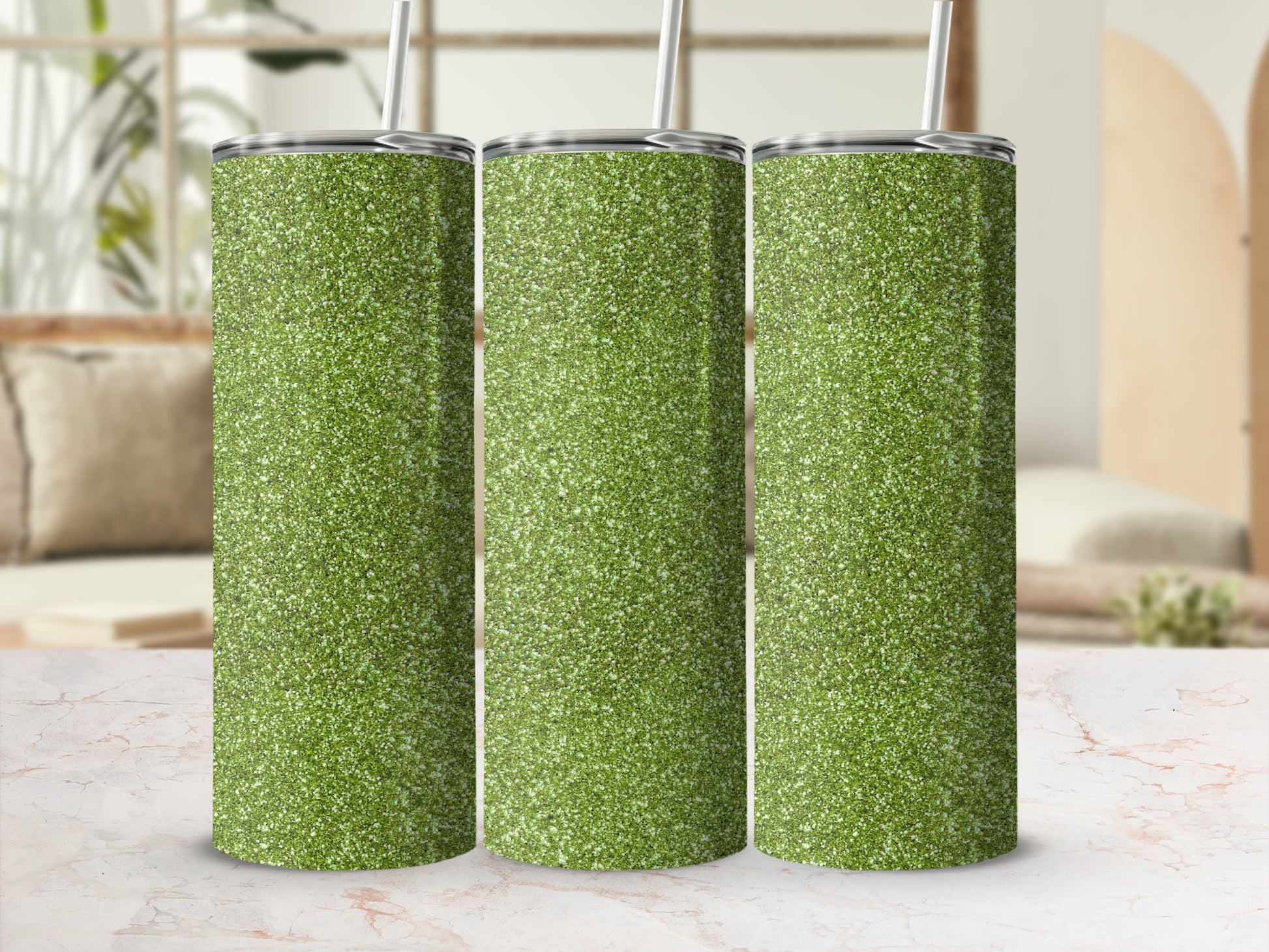 Three green glitter tumblers with straws lined up on a marble surface.