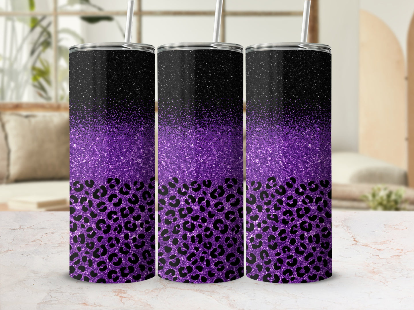 Three glitter and leopard print tumblers with straws on a marble surface.