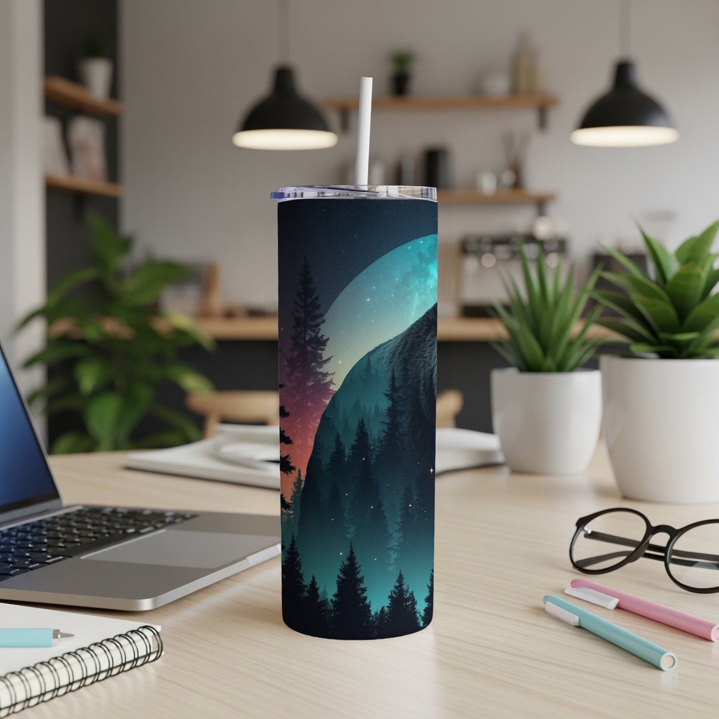 Tumbler with forest and moon design, resting on a desk.