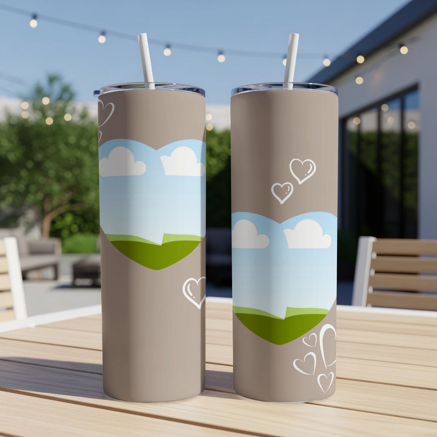 Two tan tumblers with heart and landscape designs sit on a wooden table.