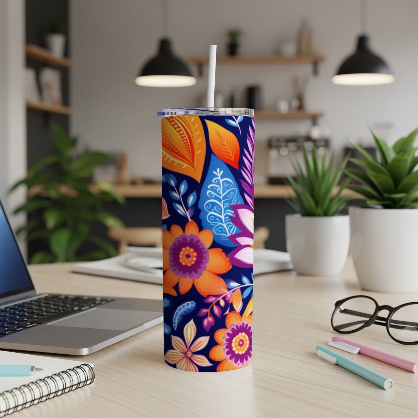 Blue tumbler with colorful floral and leaf pattern, white straw, on a desk.