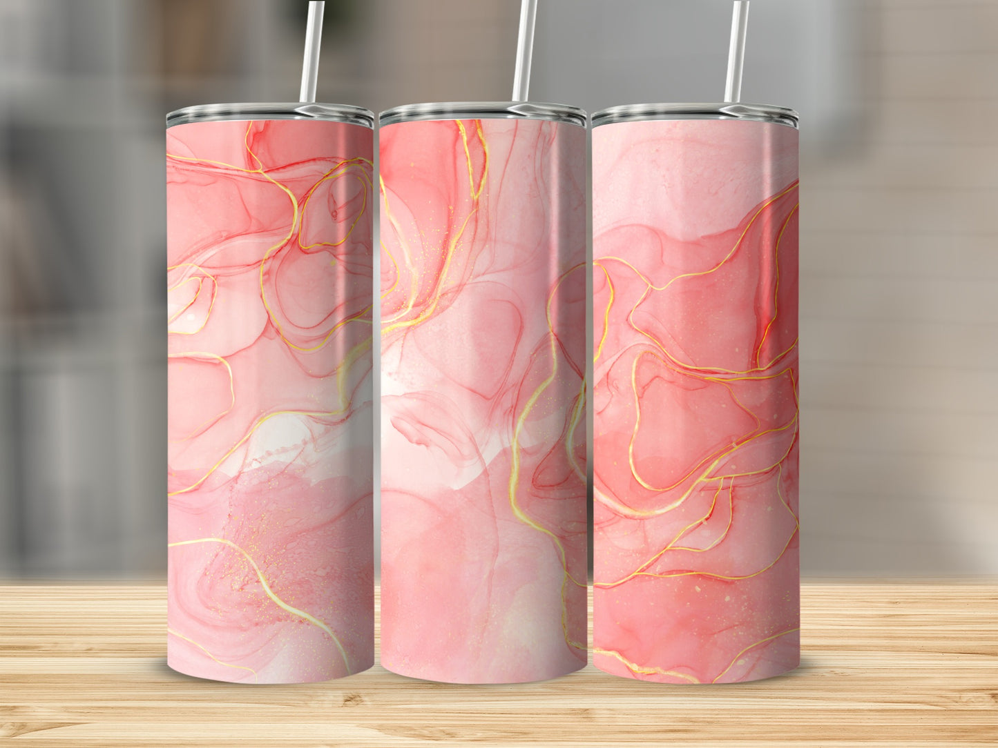 Three pink and gold abstract art tumblers with straws on a wooden surface.