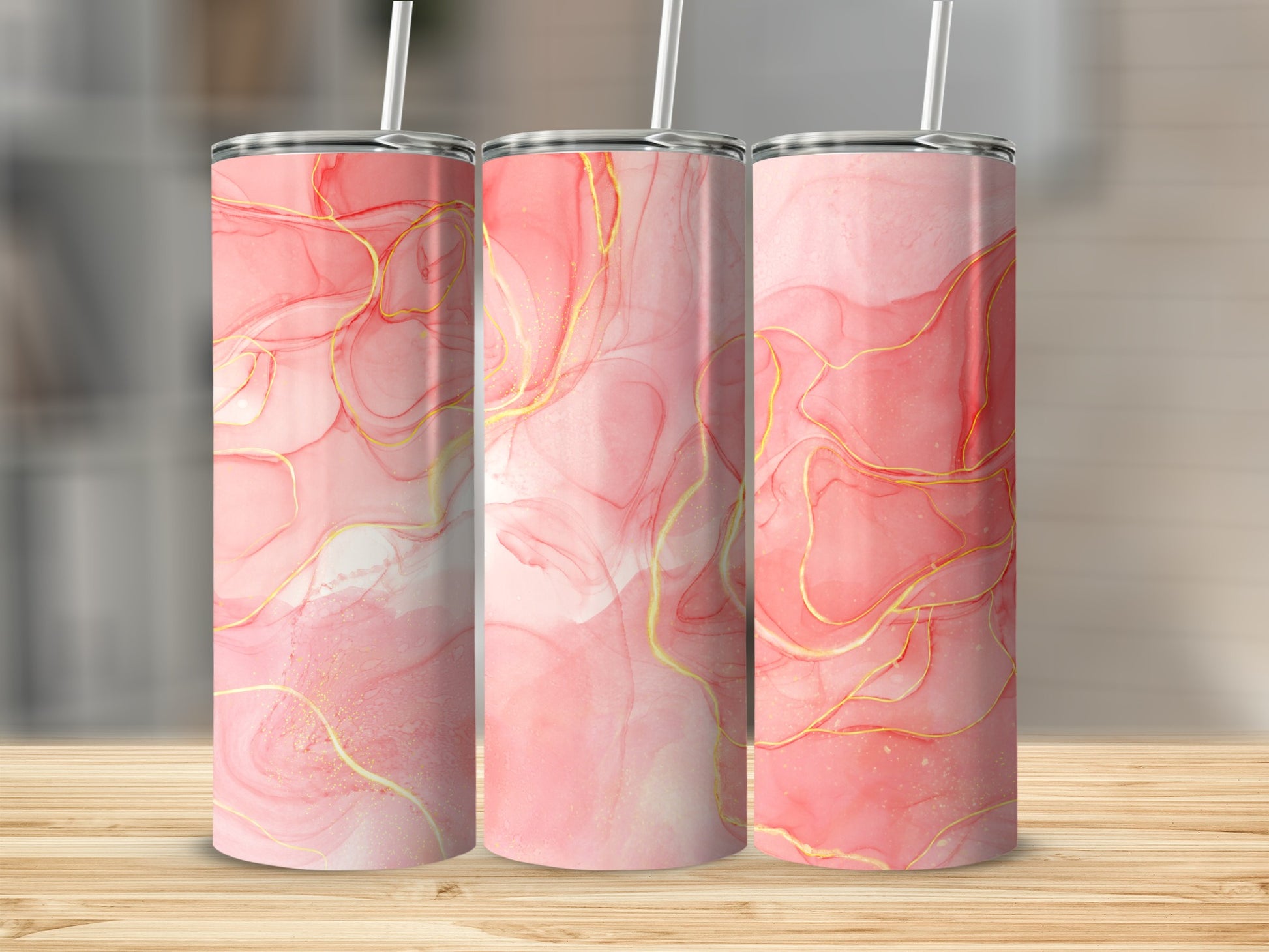 Three pink and gold abstract art tumblers with straws on a wooden surface.