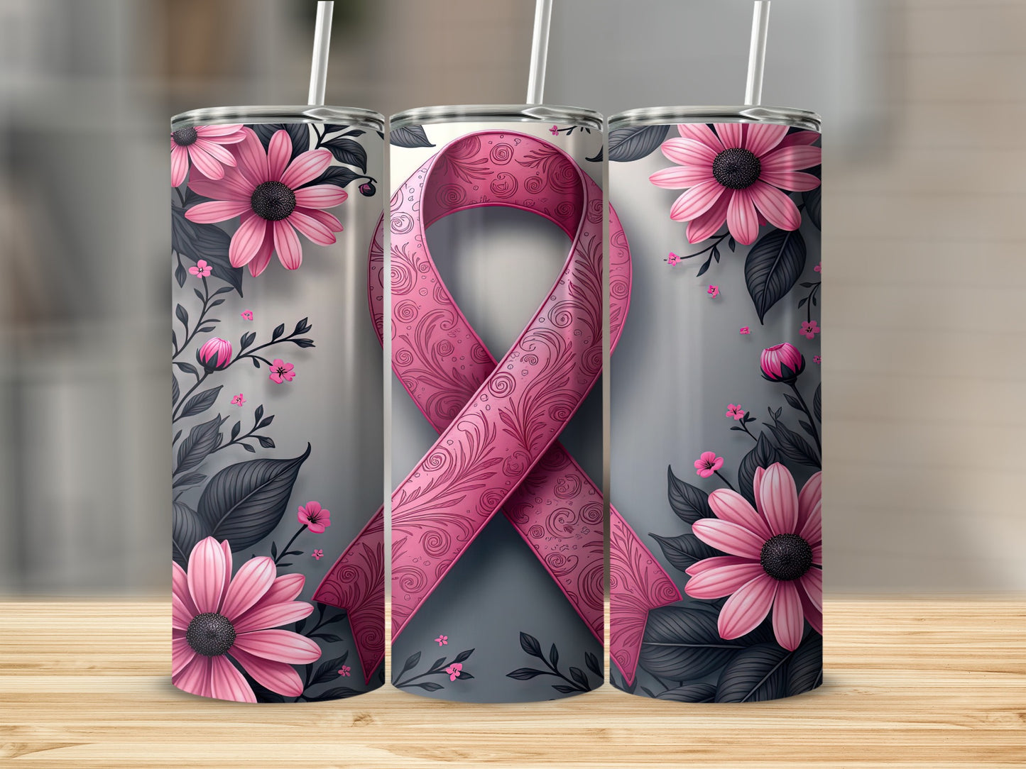 Three pink ribbon tumblers with floral designs and straws on a wooden surface.