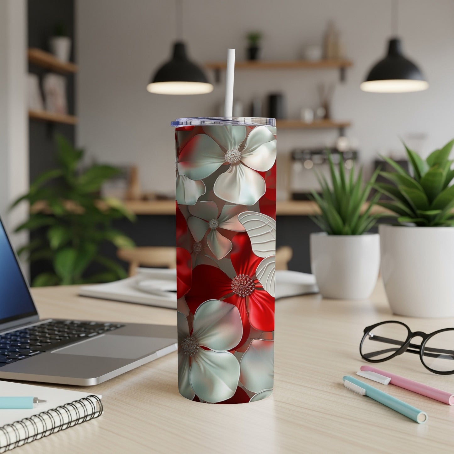 Tall stainless steel tumbler with red and white floral pattern on a desk.