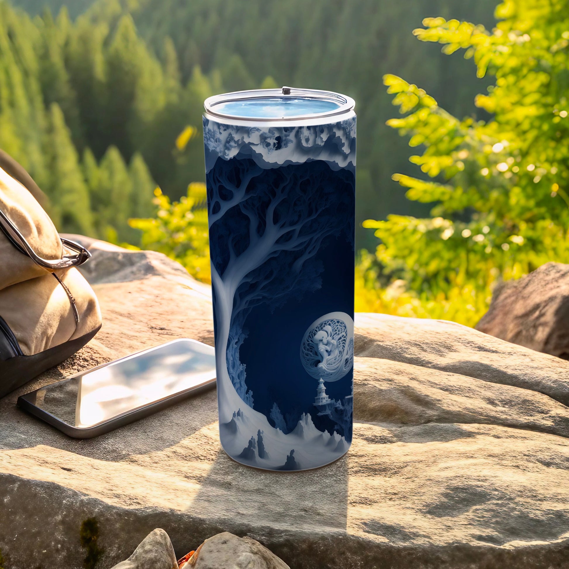 Blue fantasy landscape wrap on a tall tumbler, resting on rocks.