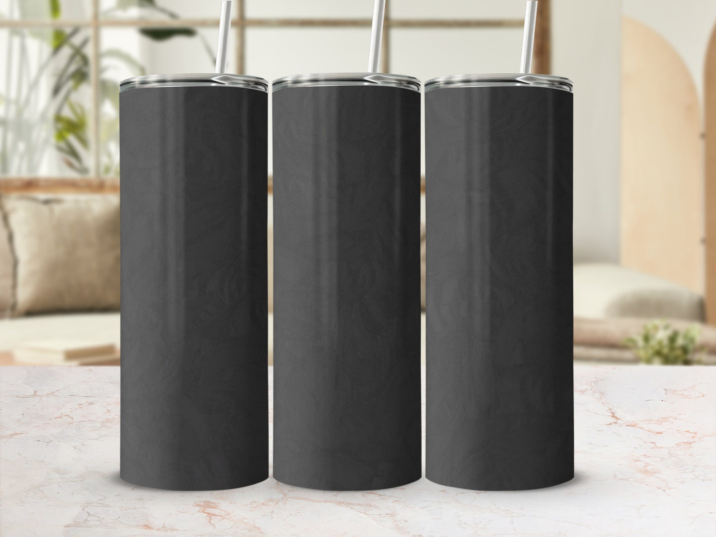 Three black tumblers with silver straws on a marble surface.
