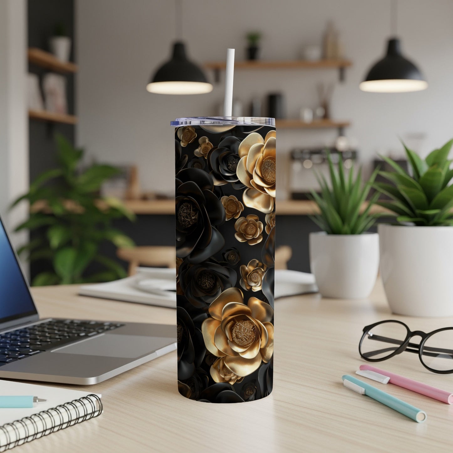 Black and gold floral patterned tumbler with straw on desk.