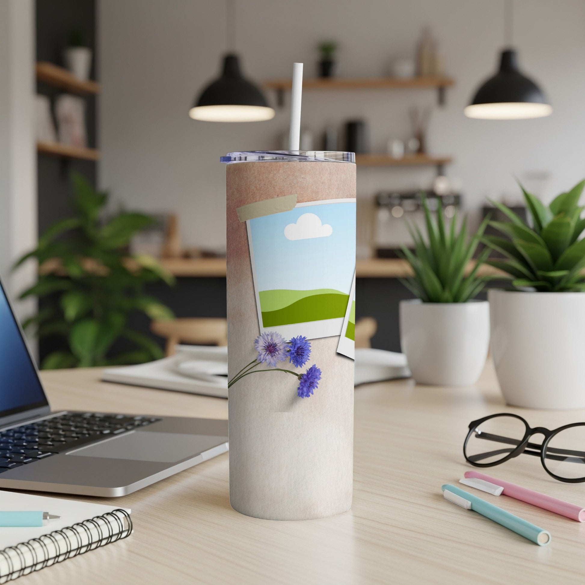 Tall tumbler with two framed pictures and blue flowers on a desk.
