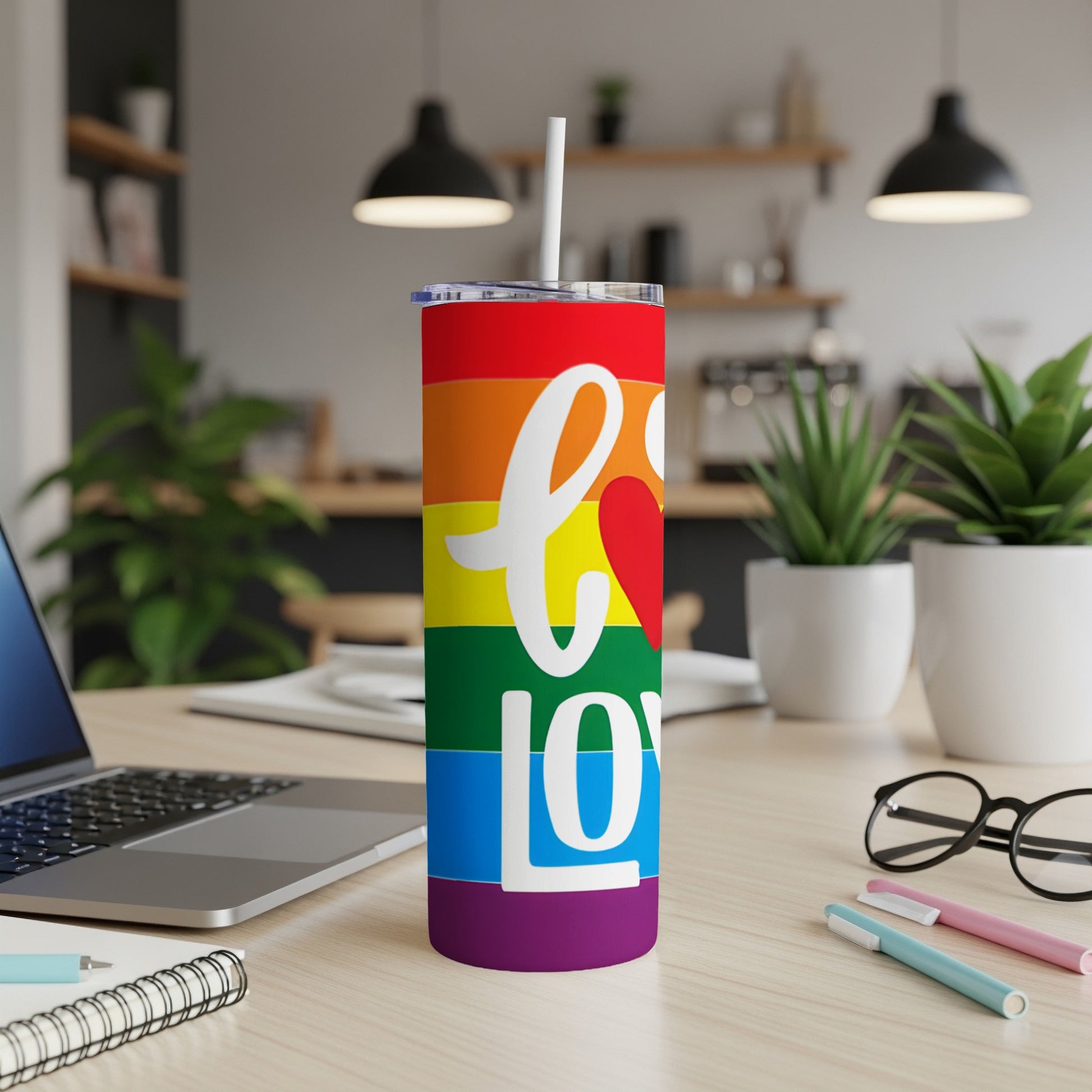 Rainbow tumbler with "love" text, featuring a straw, on a desk.
