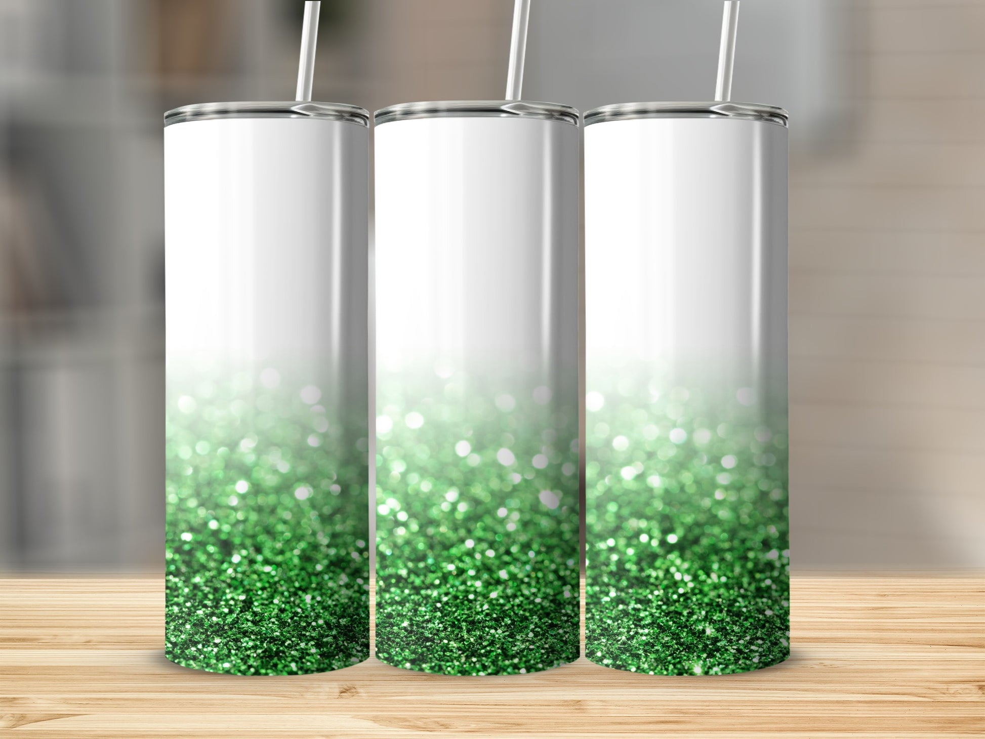 Three white tumblers with green glitter gradient and straw on wooden surface.