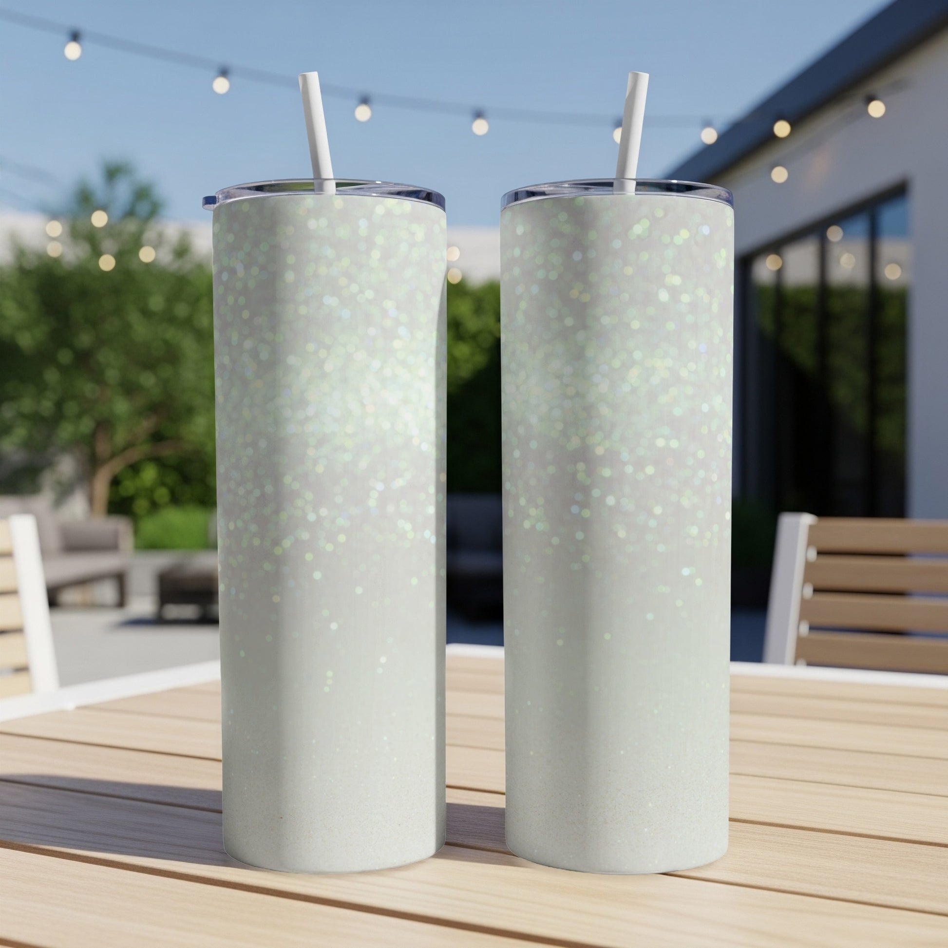 Two white glitter tumblers with straws on a wooden table outdoors.