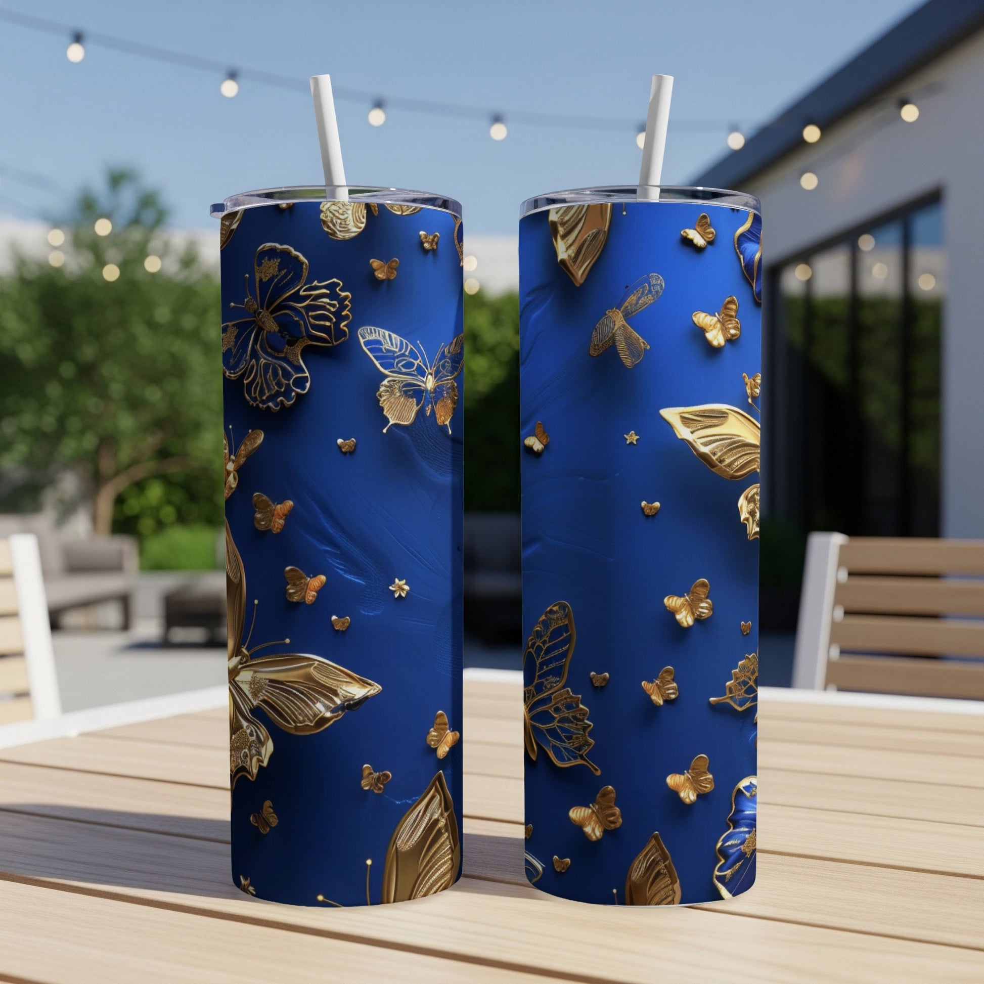Two blue tumblers with gold butterfly and leaf design on outdoor table.
