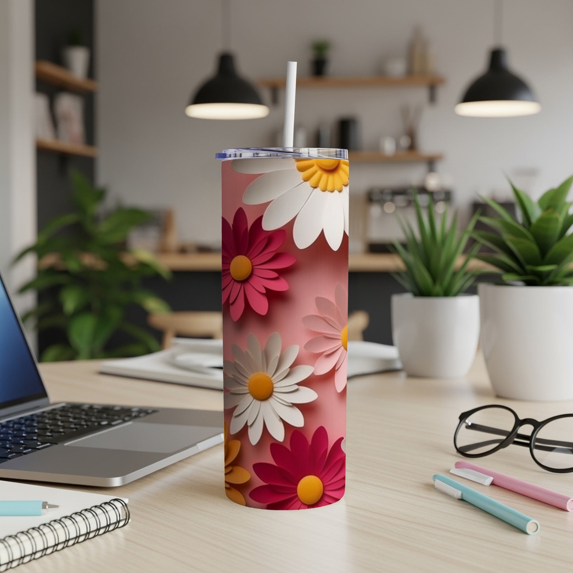 Pink tumbler with white and pink daisy floral pattern on a desk.
