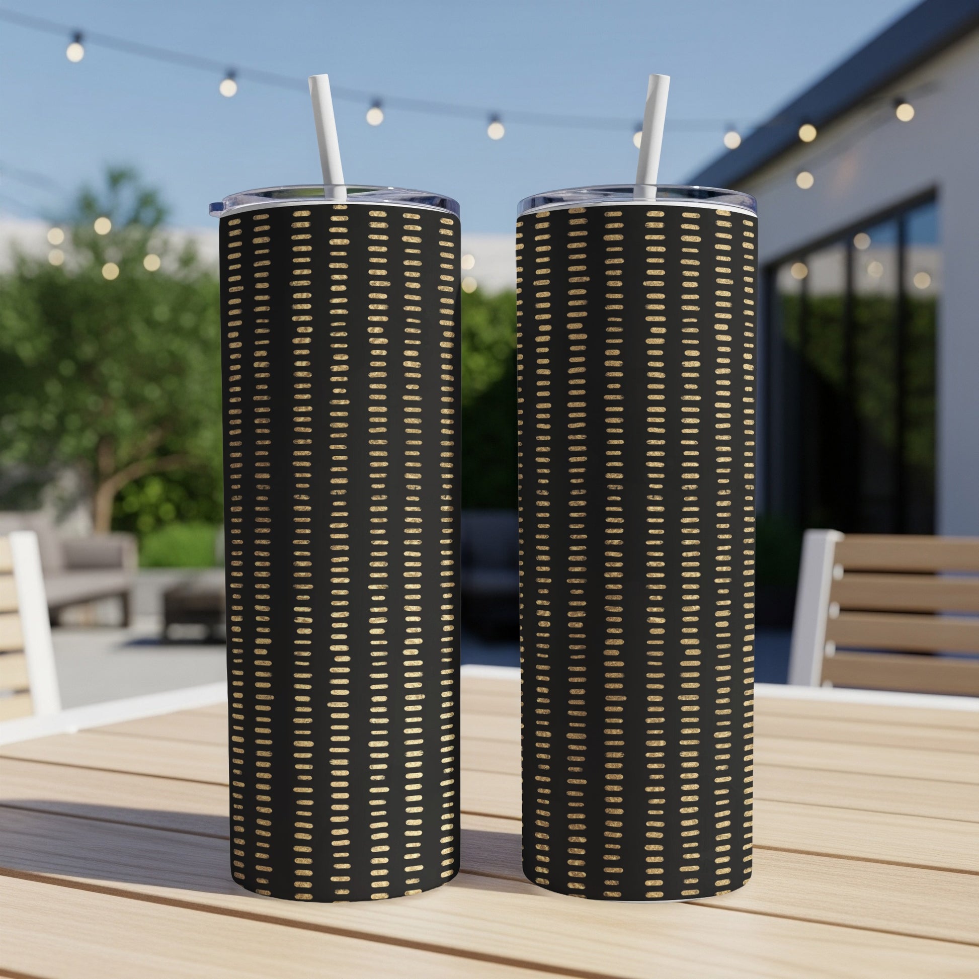 Two black tumblers with gold dash pattern and white straws on a wooden table.