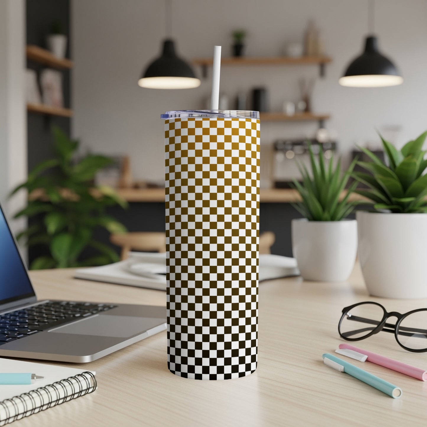 Gold and brown checkerboard tumbler with straw on a desk.