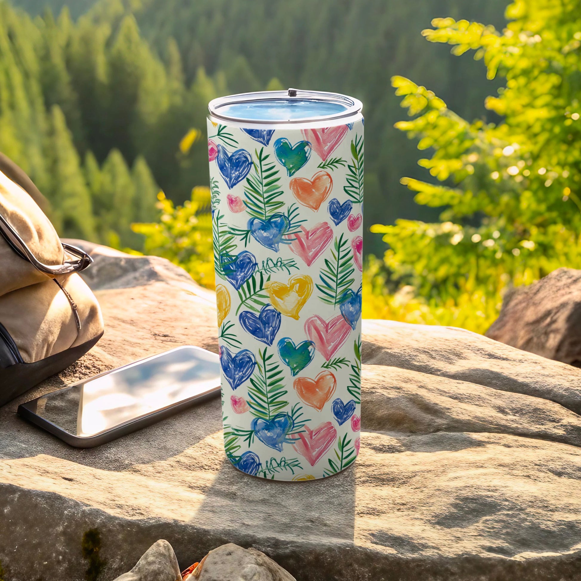 Tumbler with a watercolor heart and leaf pattern, resting on rocks.