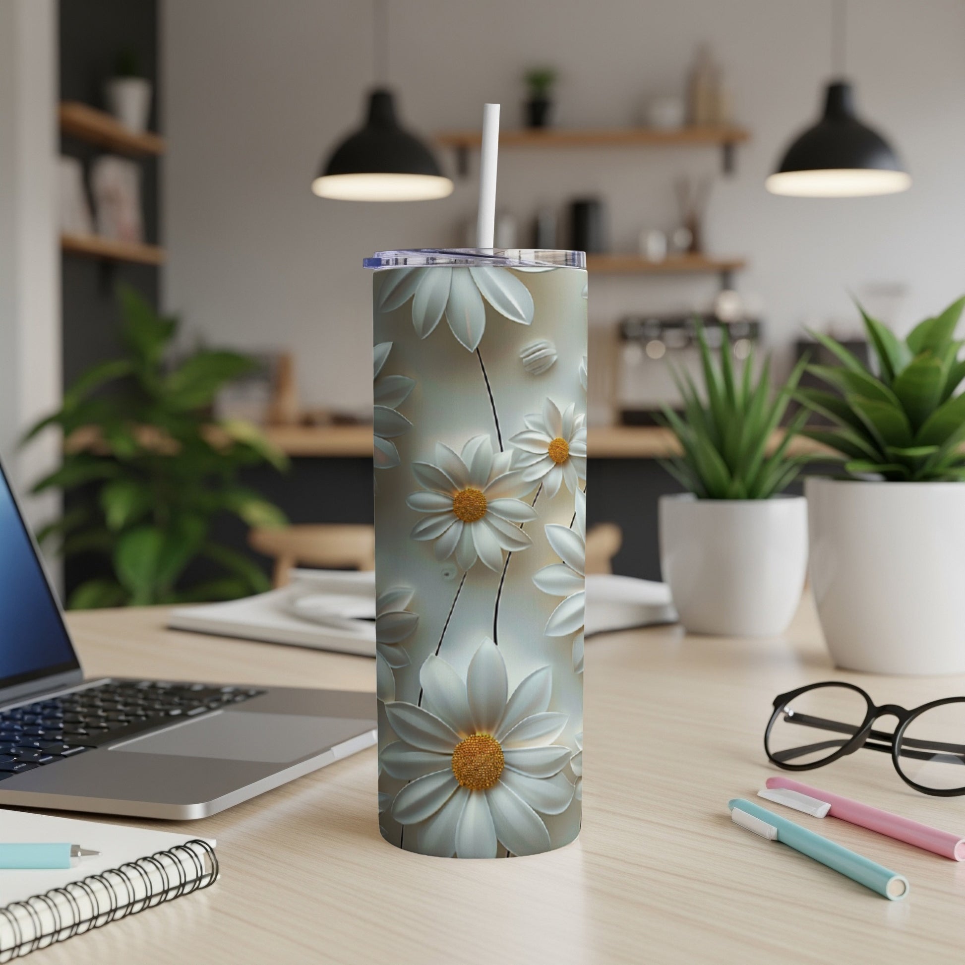 White daisy pattern on a stainless steel tumbler with straw on a desk.