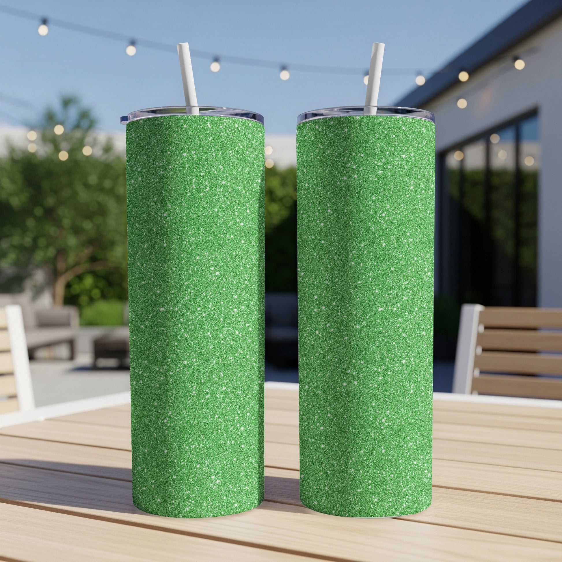 Two green glitter tumblers with white straws on a wooden table outdoors.
