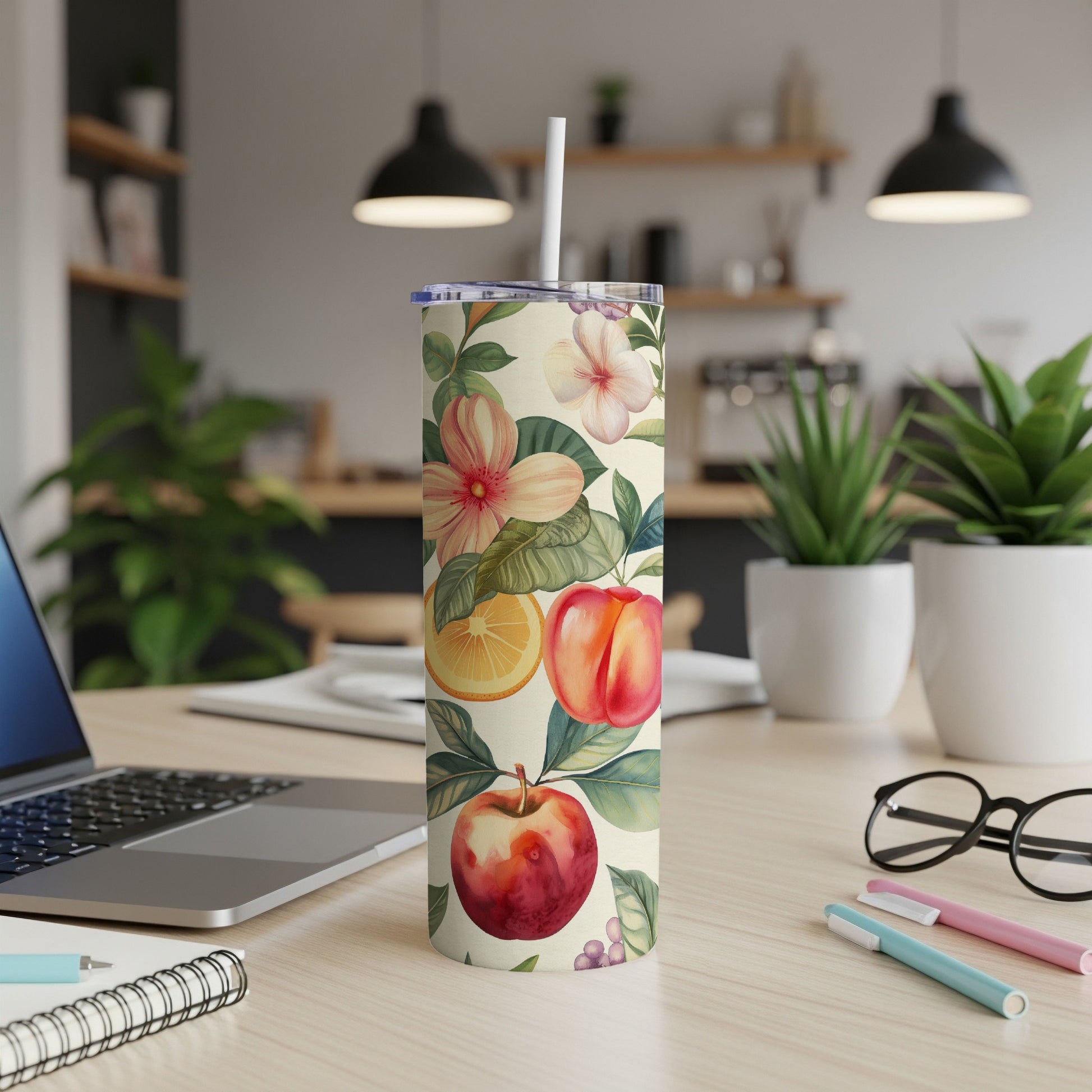 Floral and fruit patterned tumbler with straw on a desk.