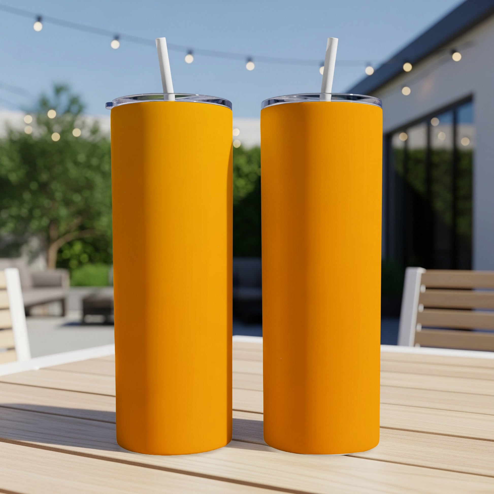 Two tall, orange tumblers with white straws sit on a wooden table outdoors.